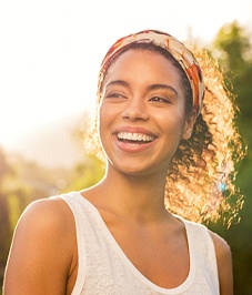 A woman wearing a white tank top and smiling while outside, showing off her new porcelain veneers