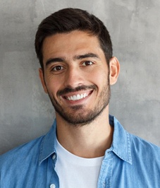 A young male wearing a white shirt and blue button-down smiling after receiving in-office teeth whitening