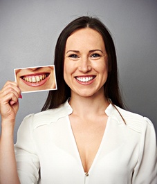Smiling woman holds photo of teeth before whitening treatment